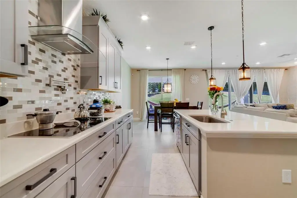 The DREAM KITCHEN is a showstopper with stylish cabinetry, stone countertops, a breakfast bar, built-in oven, cooktop stove with POT FILLER, tile backsplash, walk-in pantry, and a GALLEY-STYLE COFFEE BAR AREA—perfect for morning routines or entertaining.
