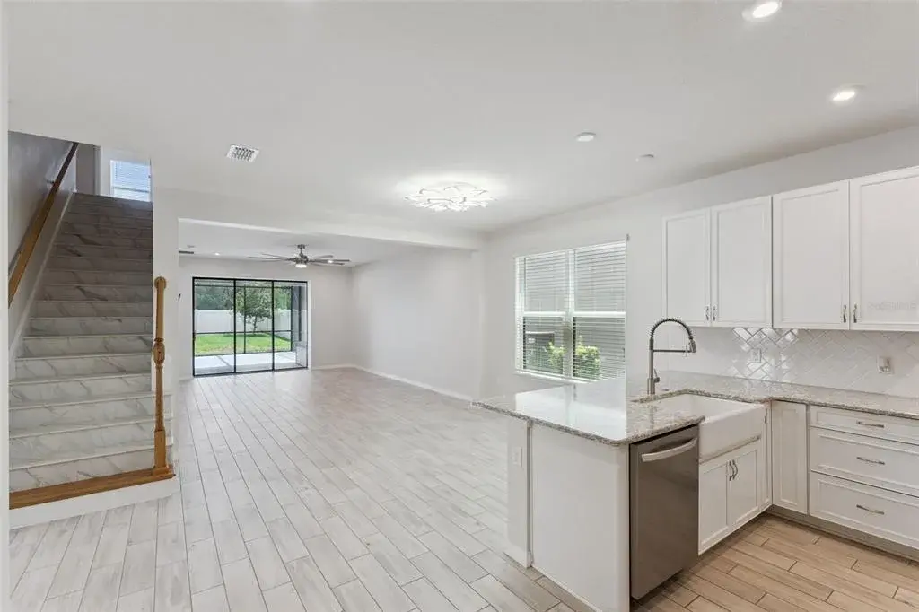 Kitchen & Main Living Area – Wide view highlights the home's open layout, with the kitchen flowing into the spacious living area and sliding glass doors extending the sightline to the screened patio and backyard.