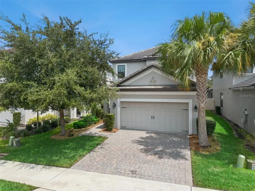 Wide exterior view highlights the two-story design, tile roof, established landscaping, palm trees, and attractive paver driveway.