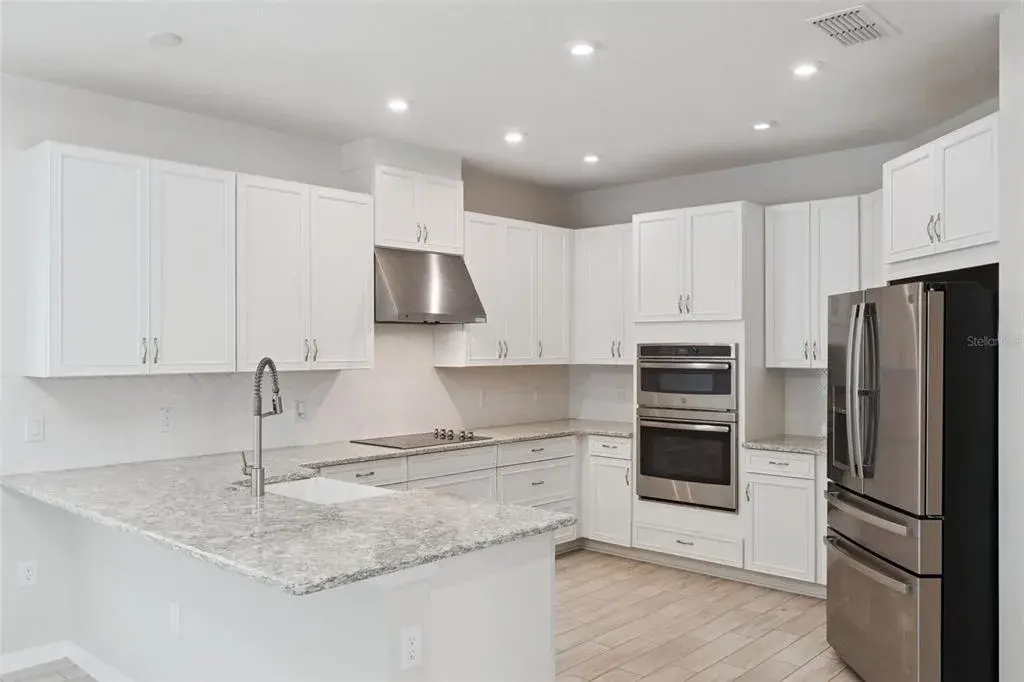 Kitchen – Bright kitchen features abundant white cabinetry, granite countertops, a tile backsplash, recessed lighting, stainless steel appliances, double wall ovens, and generous counter space for everyday prep.