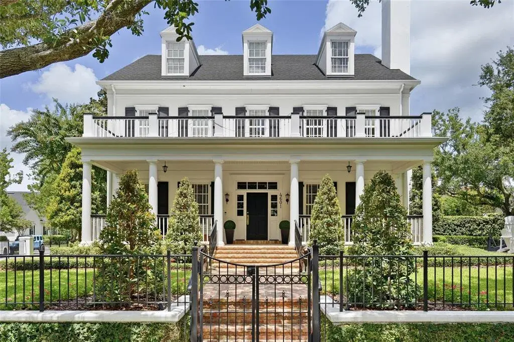 A striking front elevation showcases the home’s symmetrical design, expansive covered porch, upper balcony and beautifully manicured landscaping.
