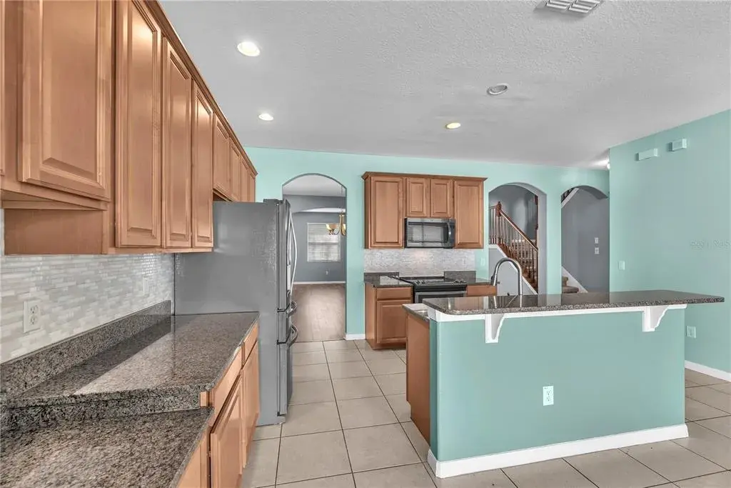 Designed to impress, the kitchen features polished granite countertops, a large center island with an undermount sink, rich 42-inch maple cabinetry with roll-out shelves, a spacious pantry, breakfast bar, built-in desk, sunny breakfast nook, and stainless steel appliances, including a built-in microwave, glass-top range, and side-by-side refrigerator.
