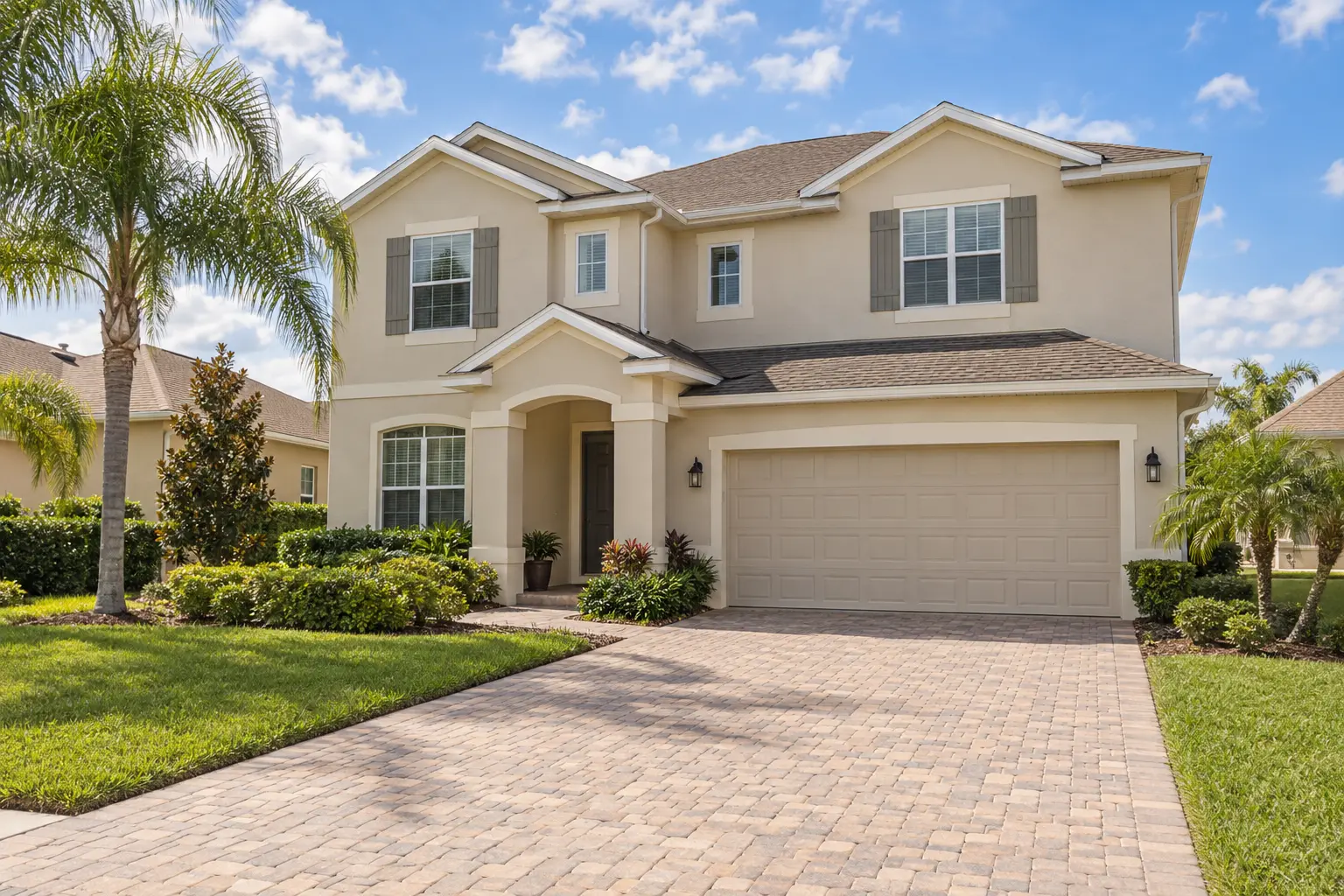 Illustrative Kissimmee-style detached home with a paved driveway, attached garage, pale stucco exterior and tropical landscaping.