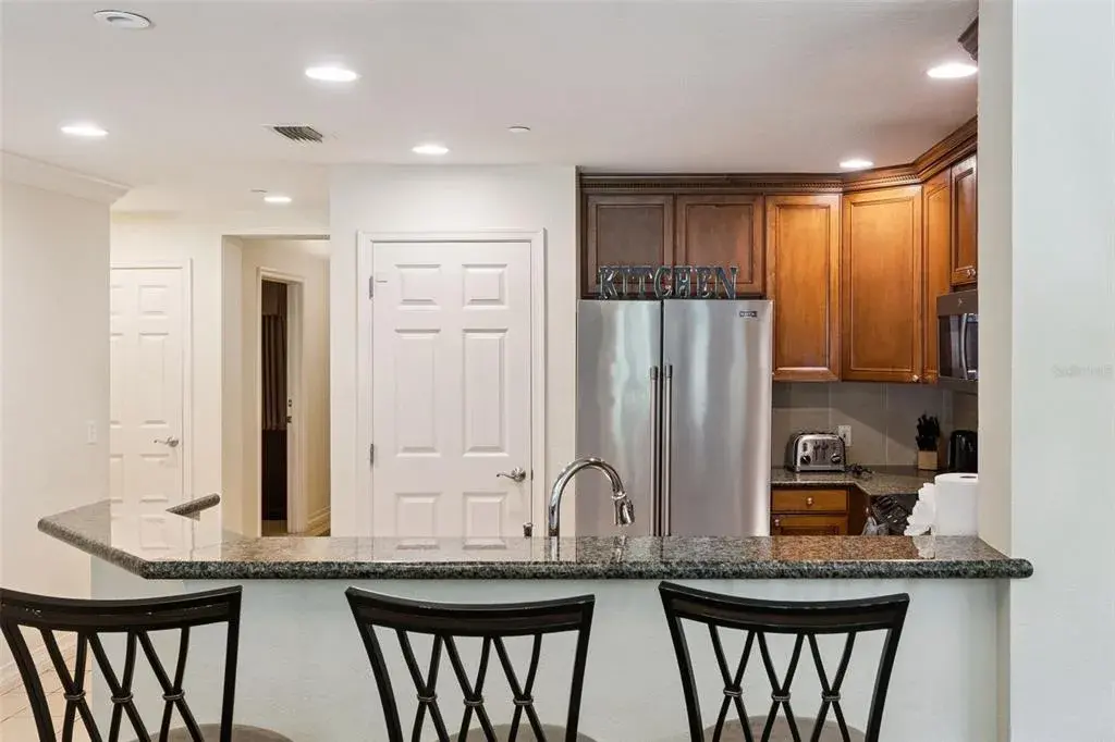 Breakfast Bar & Kitchen: Raised granite breakfast bar ideal for casual seating, featuring a stainless steel refrigerator, recessed lighting, and a pantry door.