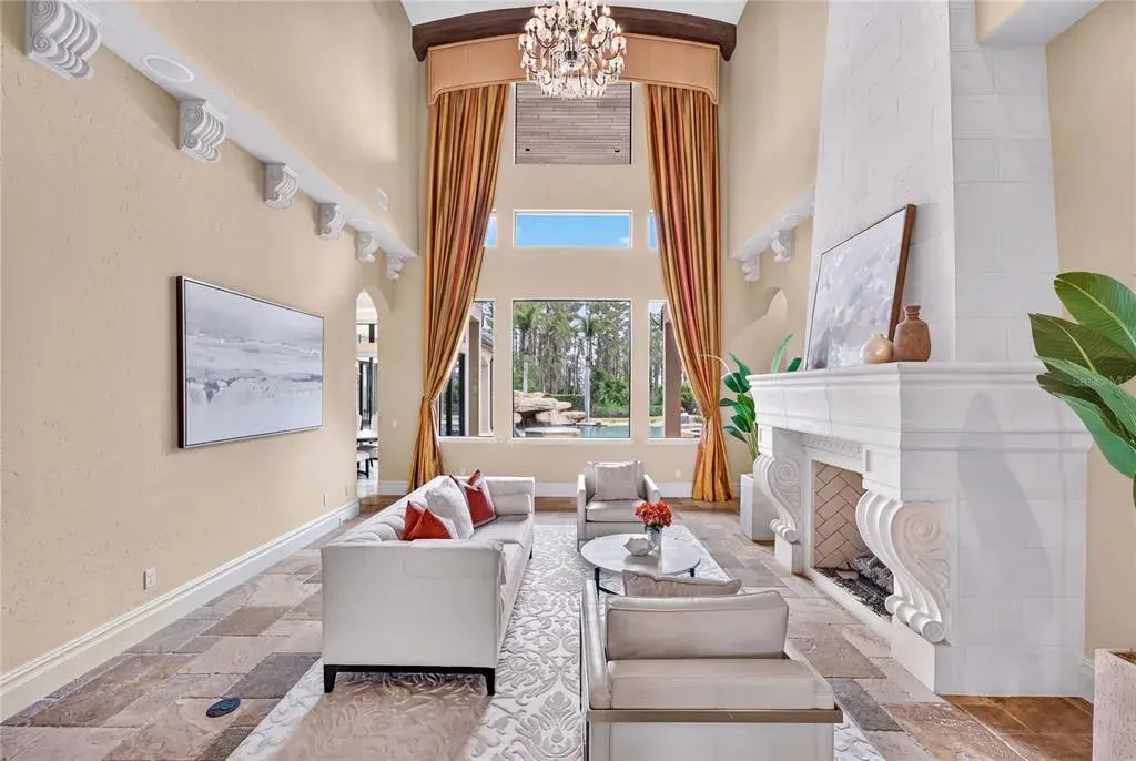 The foyer opens to a two-story travertine-tiled formal living area with dramatic fireplace and towering picture windows that frame the view of the pool and lake.