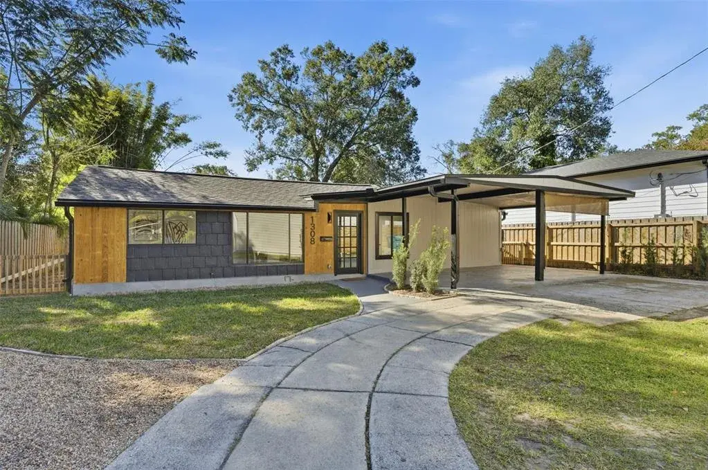 Modern single-story residence set back on a private lot with a curved walkway, covered carport, wood-accent exterior details, and newly fenced grounds.