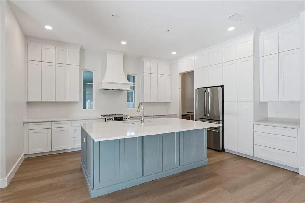 The main kitchen features a blue island, white cabinetry, a statement range hood, and stainless steel appliances.