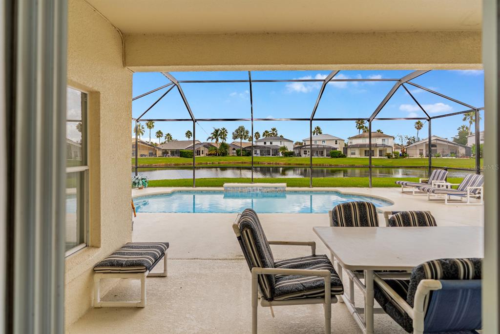 Covered lanai with outdoor dining space, overlooking the screened-in pool and spa with tranquil pond views—ideal for entertaining or relaxing in the Florida sunshine