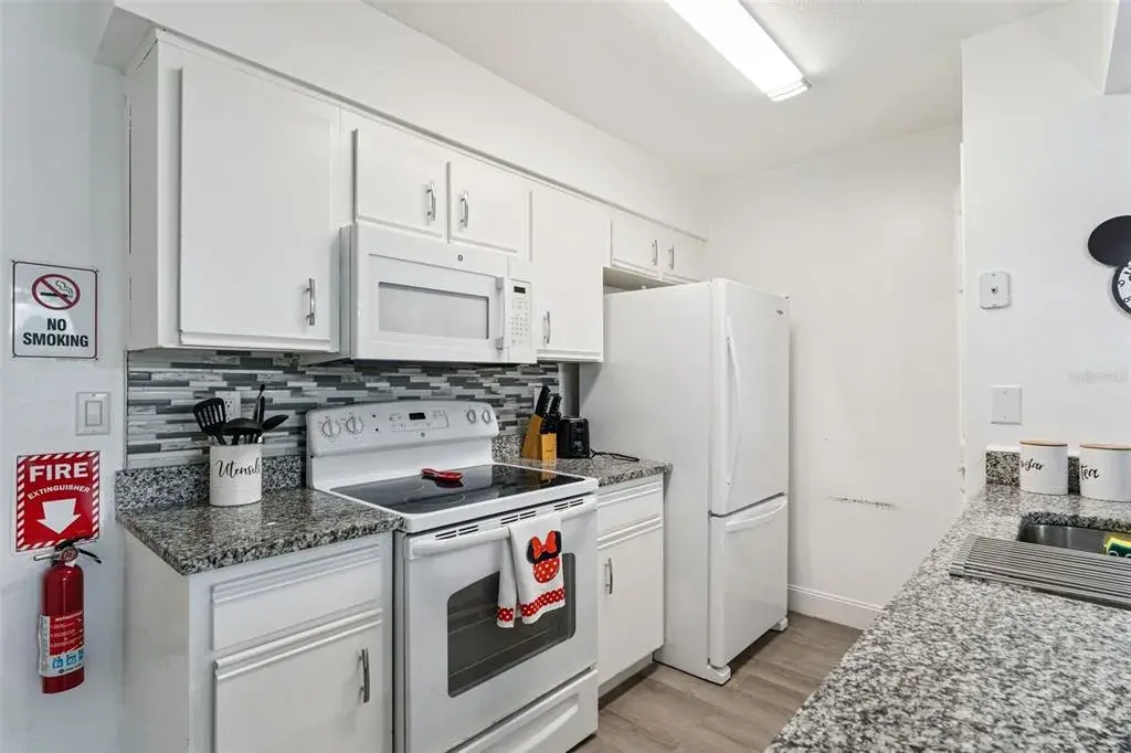 Kitchen Interior: Bright kitchen equipped with clean white cabinetry, granite countertops, a mosaic tile backsplash, electric range, and matching white appliances.