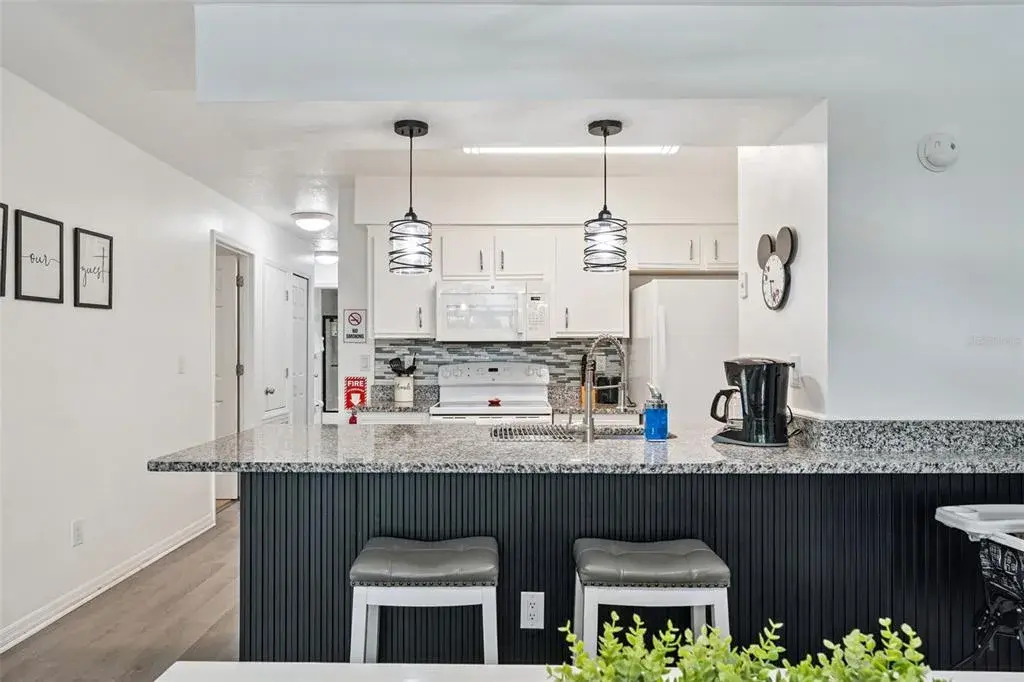 Breakfast Bar Seating: Custom vertical-slat accent breakfast bar with granite countertop overhang, stool seating, and updated pendant light fixtures.