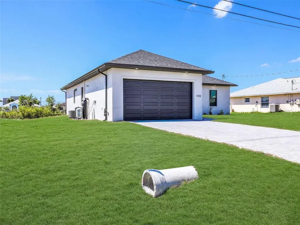 Contemporary single-story residence featuring a dark gray garage door, white exterior siding, and a dark shingle roof the color of the grass has been virtually enhanced