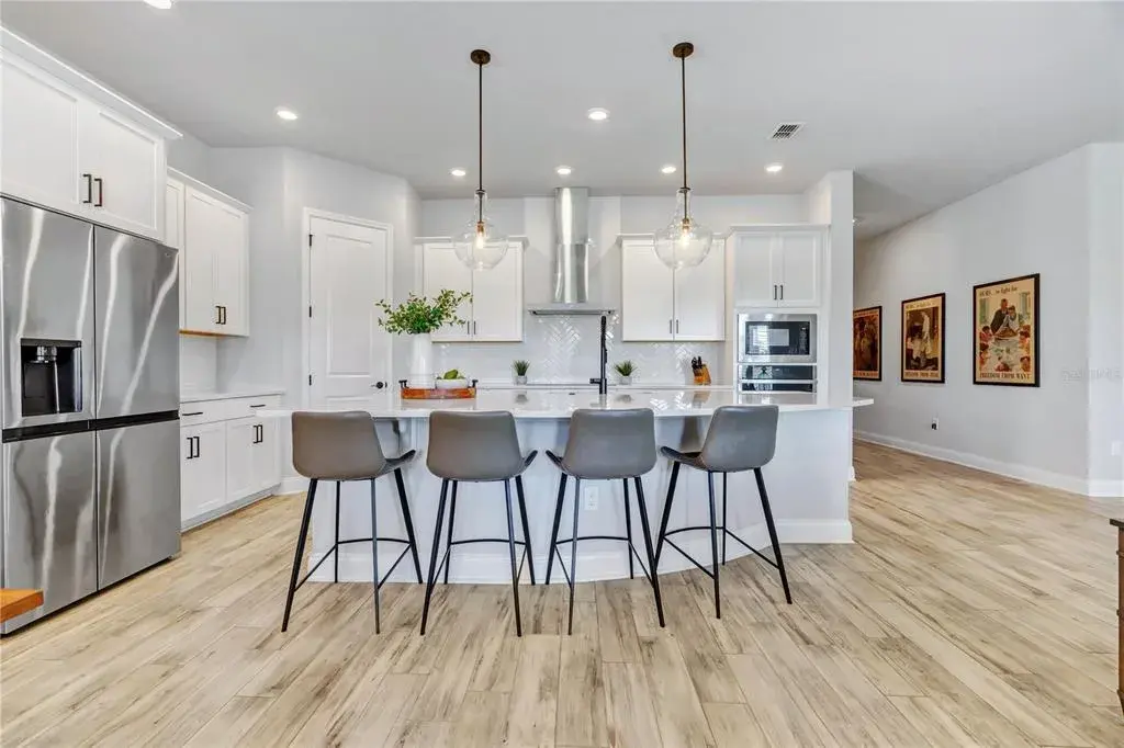 Chef inspired kitchen with an expansive Calacatta Arno quartz island, seating for four, statement pendants, stainless appliances, and a built in wall oven and microwave.