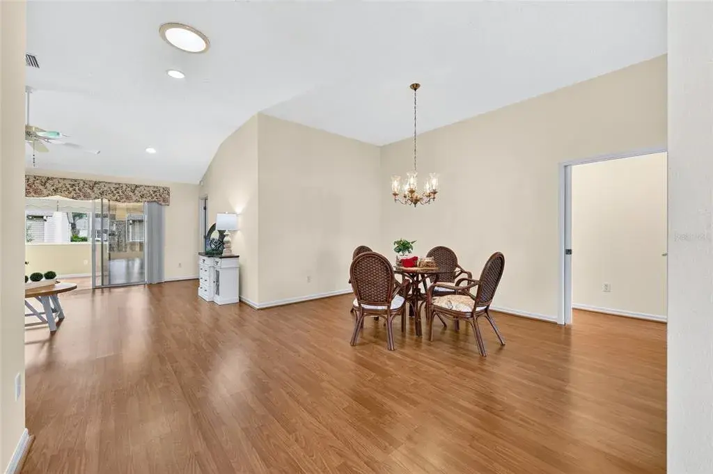 Spacious dining area featuring wood-look flooring, vaulted ceilings, a decorative chandelier, and an open layout that flows into the living space.