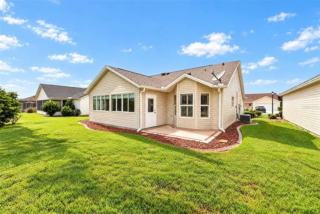 Rear exterior showcasing a spacious lawn, mature landscaping, attractive rooflines, and a convenient rear entry with a decorative patio area.