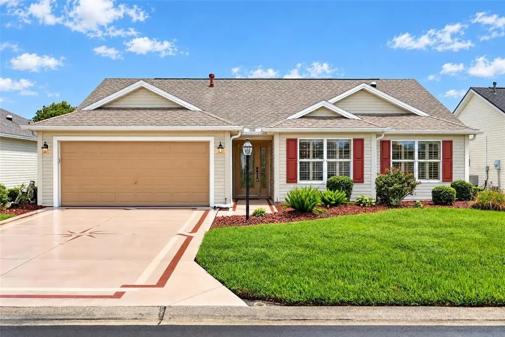 Welcoming front elevation featuring a two-car garage, decorative driveway accents, attractive landscaping, and charming red shutters.