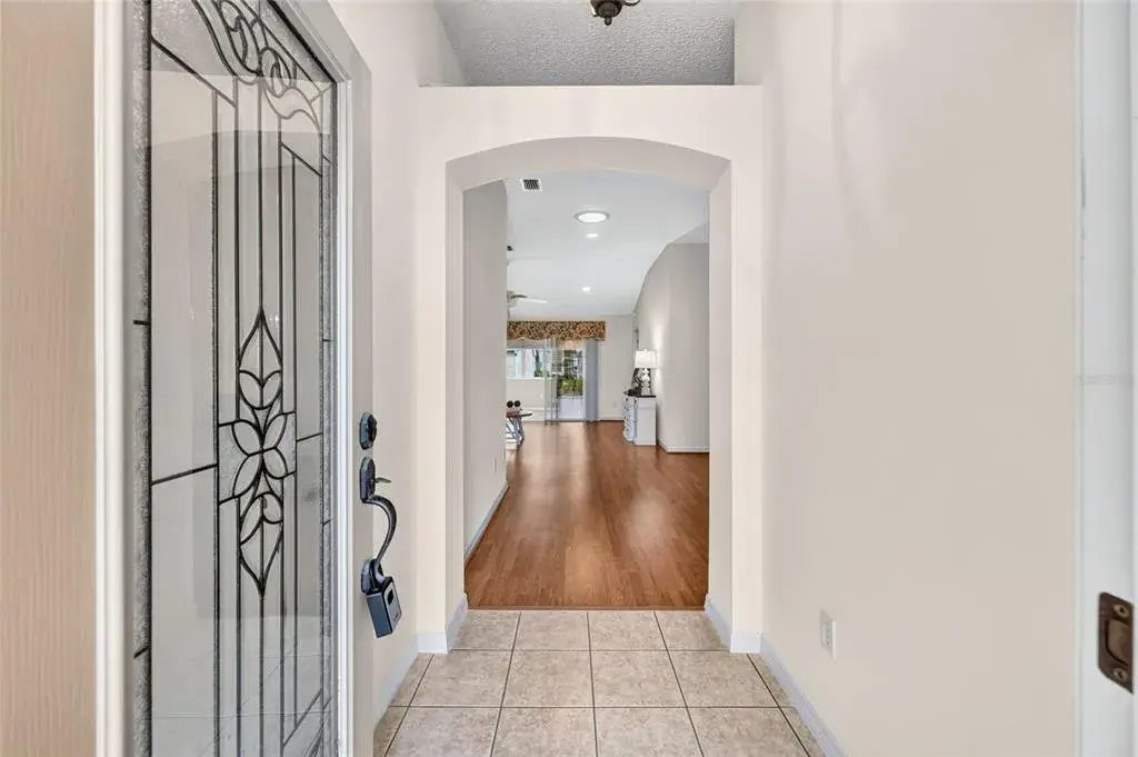 Inviting foyer featuring a decorative glass front door, tile flooring, and an elegant arched opening leading into the main living area.