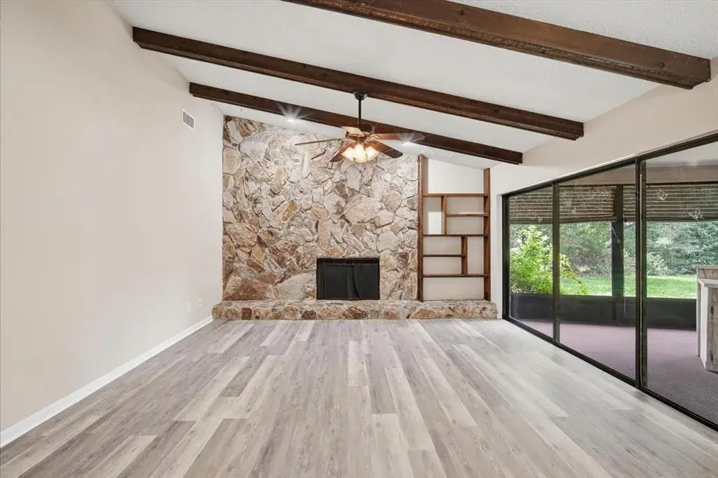 Impressive family room with soaring ceilings with stone fireplace, beams and triple sliding glass doors