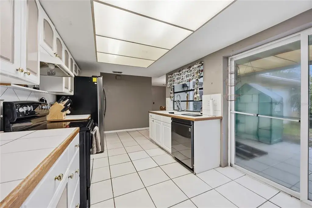 Functional kitchen featuring white cabinetry, tile flooring, updated appliances, and sliding glass door access directly to the screened lanai.