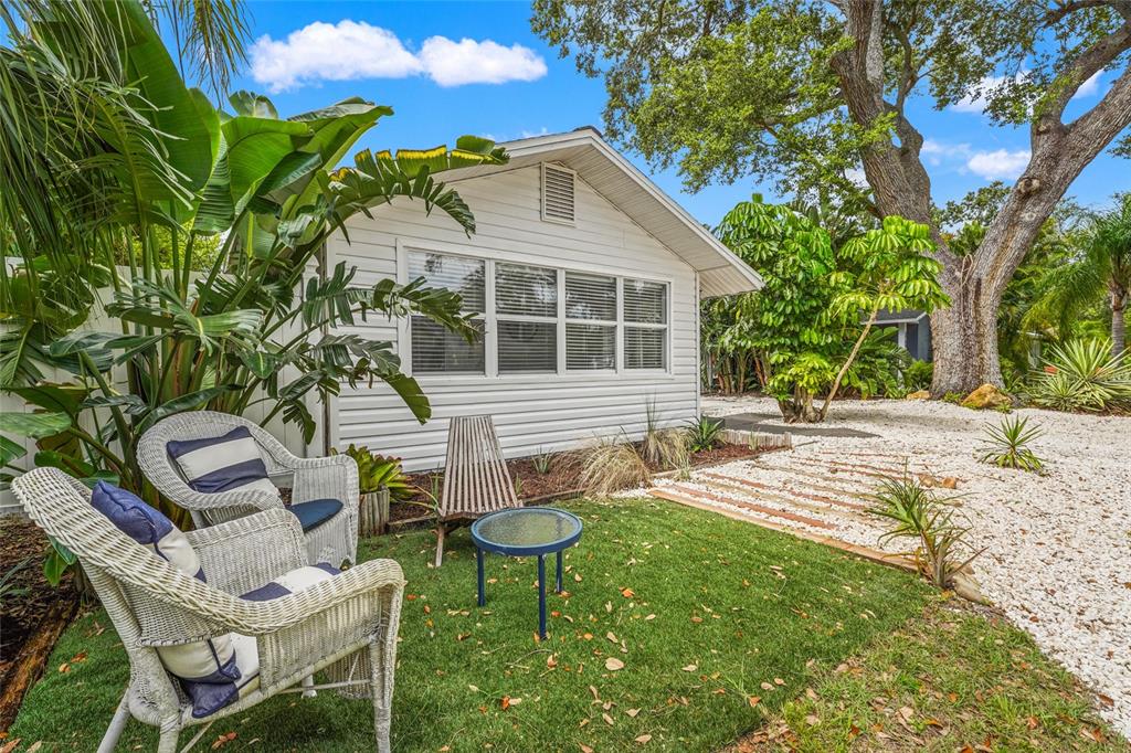 Front Elevation – This charming 1925 bungalow makes a great first impression with tropical landscaping, a wide circular shell drive, and a private seating area nestled under mature palms.