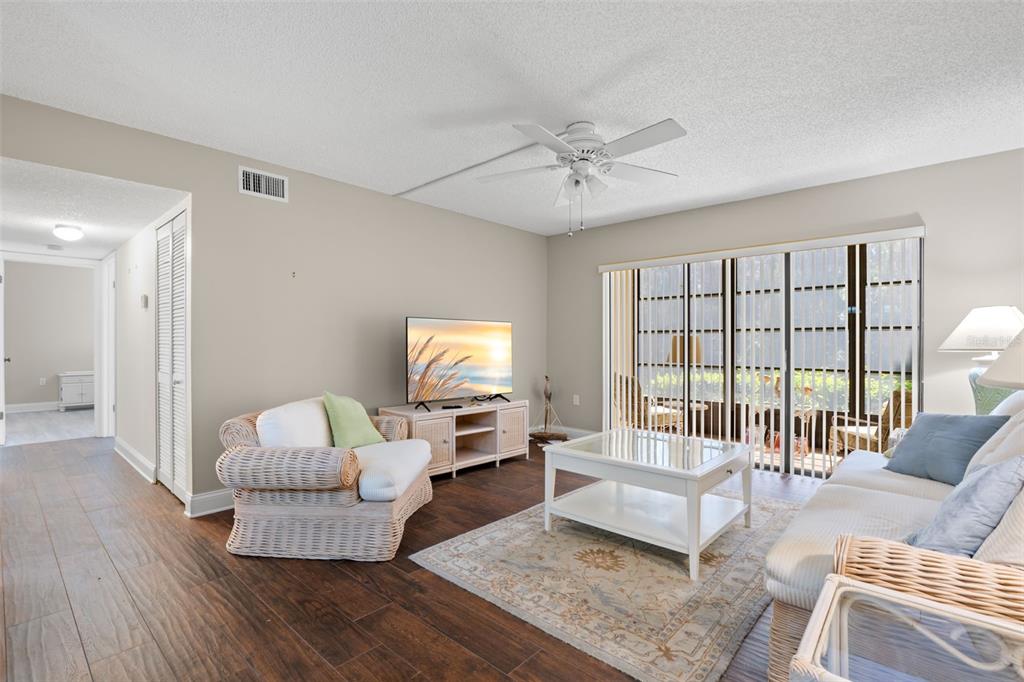 The living room features 2021 wood-look tile flooring, a ceiling fan, and wide sliding glass doors that open to the screened lanai and preserve view beyond.