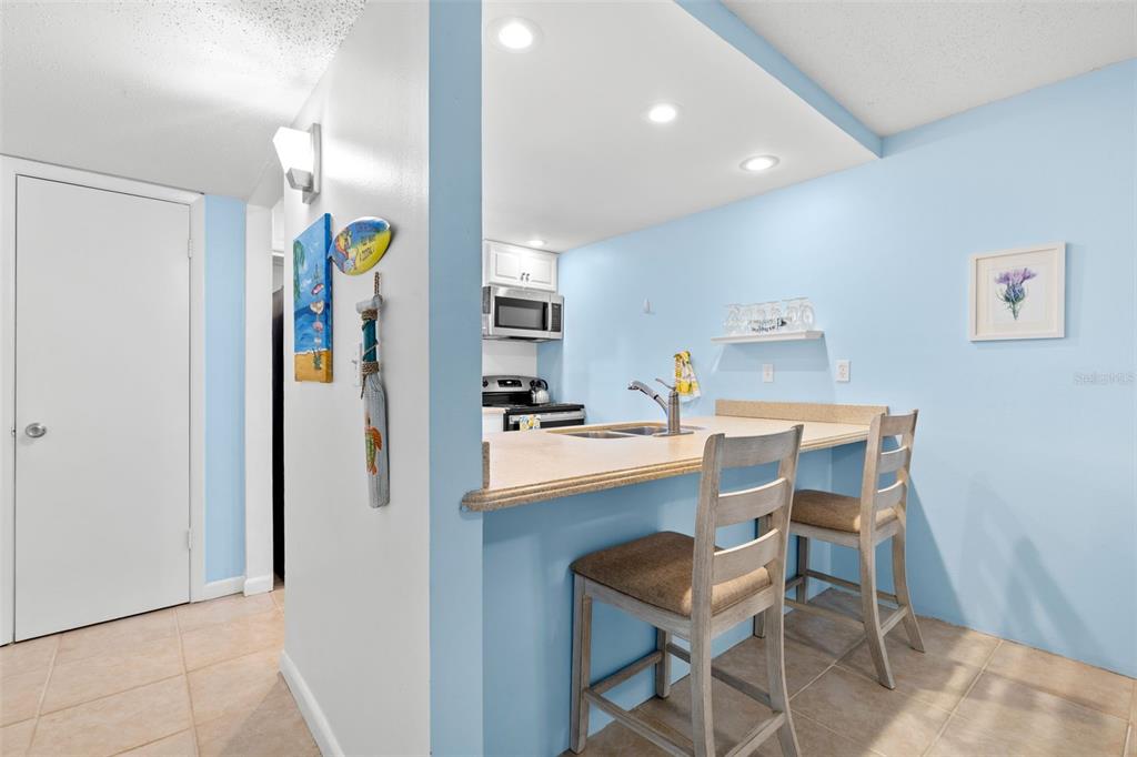 A closer look from the dining area shows the breakfast bar with seating for two, while the kitchen’s recessed lighting, Corian counters and open pass-through keep the space bright and connected to the rest of the condo.