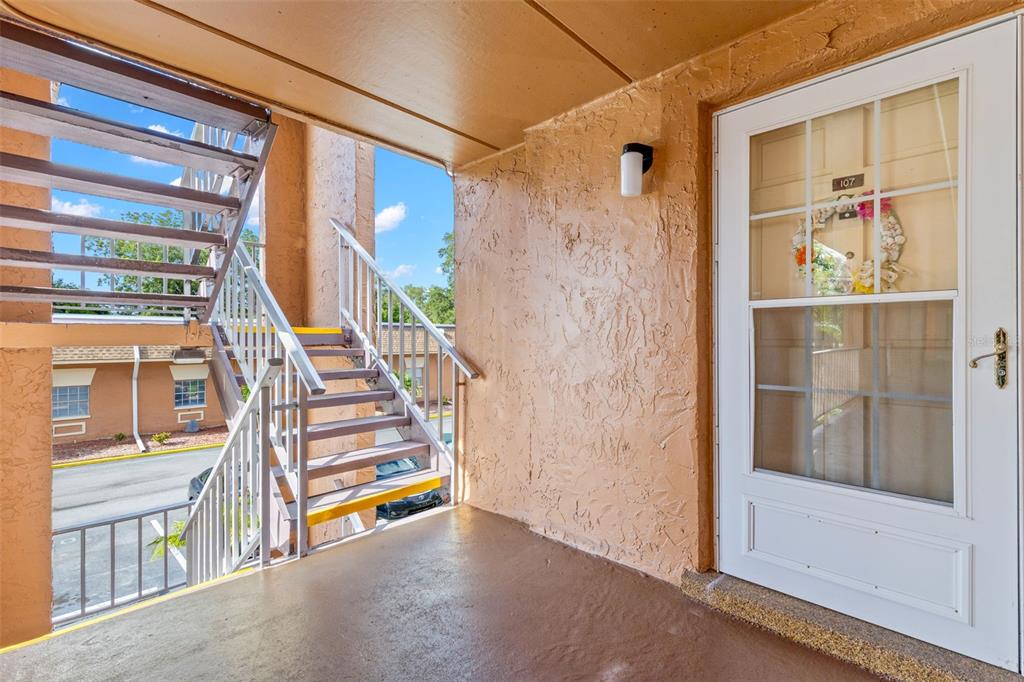 The covered exterior landing leads to a sheltered front entry, where a storm door adds another layer of light and ventilation before stepping inside.