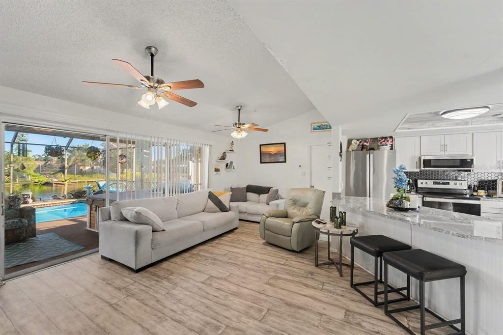 Open-concept living with pool view, modern kitchen, and ceiling fans