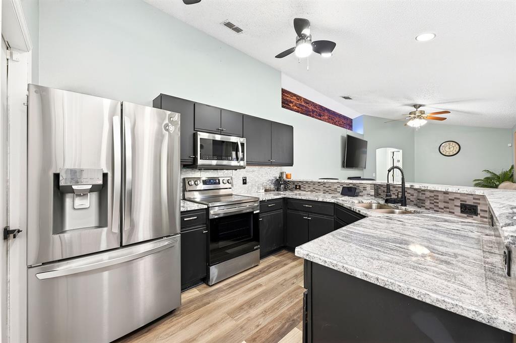 The open kitchen is ready for everything from busy mornings to entertaining, featuring STAINLESS STEEL APPLIANCES, modern neutral countertops, a decorative backsplash, and two pantries providing exceptional storage.