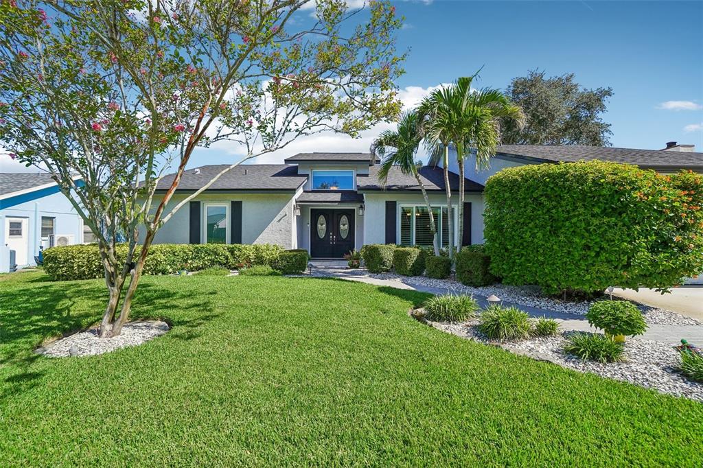 Front Exterior – Mature palms, a flowering tree, lush lawn, and neatly shaped shrubs create an inviting setting along the home’s front elevation.