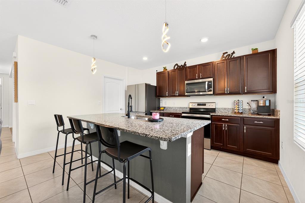 he open kitchen is both functional and inviting, featuring rich cabinetry, granite countertops, STAINLESS STEEL APPLIANCES, a large ISLAND with bar seating, and an impressive WALK-IN PANTRY offering plenty of prep and storage space!