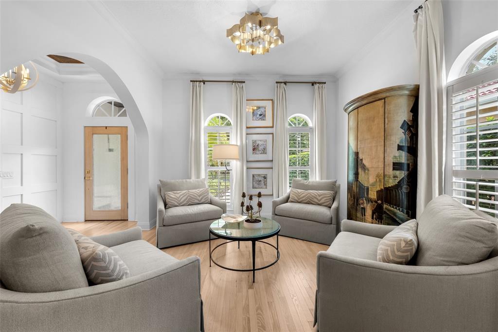 Sitting area with arched windows, plantation shutters, crown molding, and a crystal-style pendant fixture.