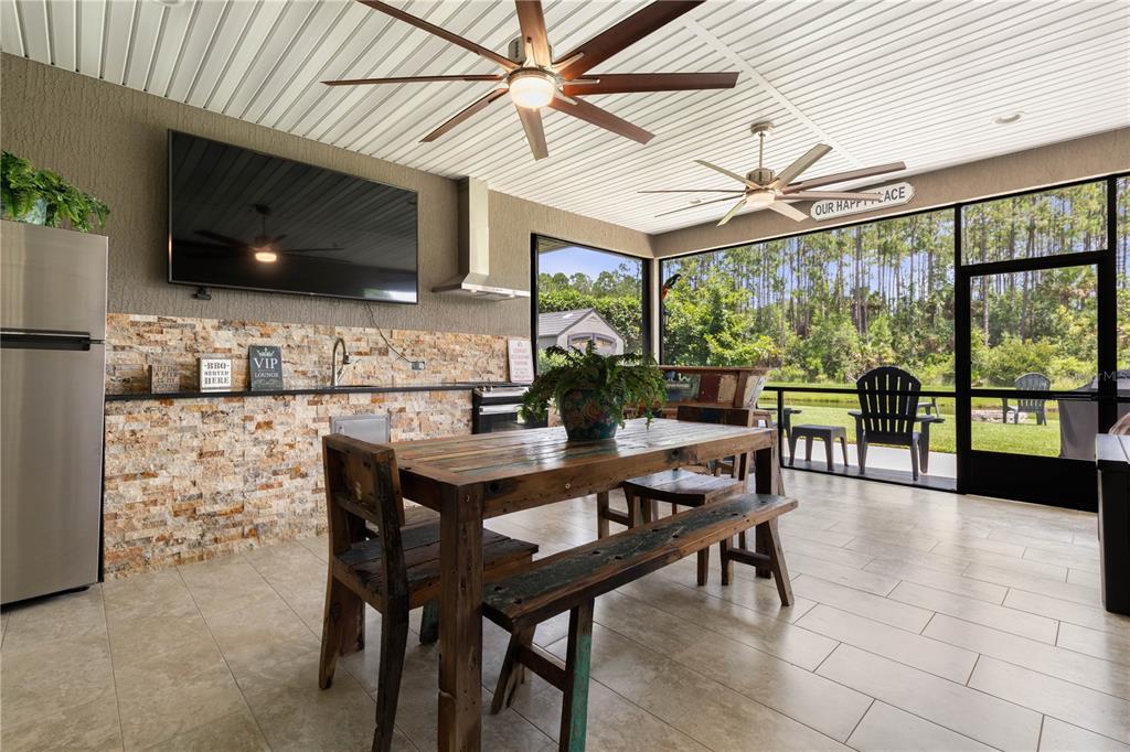 Perfect for game days and entertaining, this spacious covered outdoor living area features a large TV, full outdoor kitchen, and plenty of seating with serene wooded views.