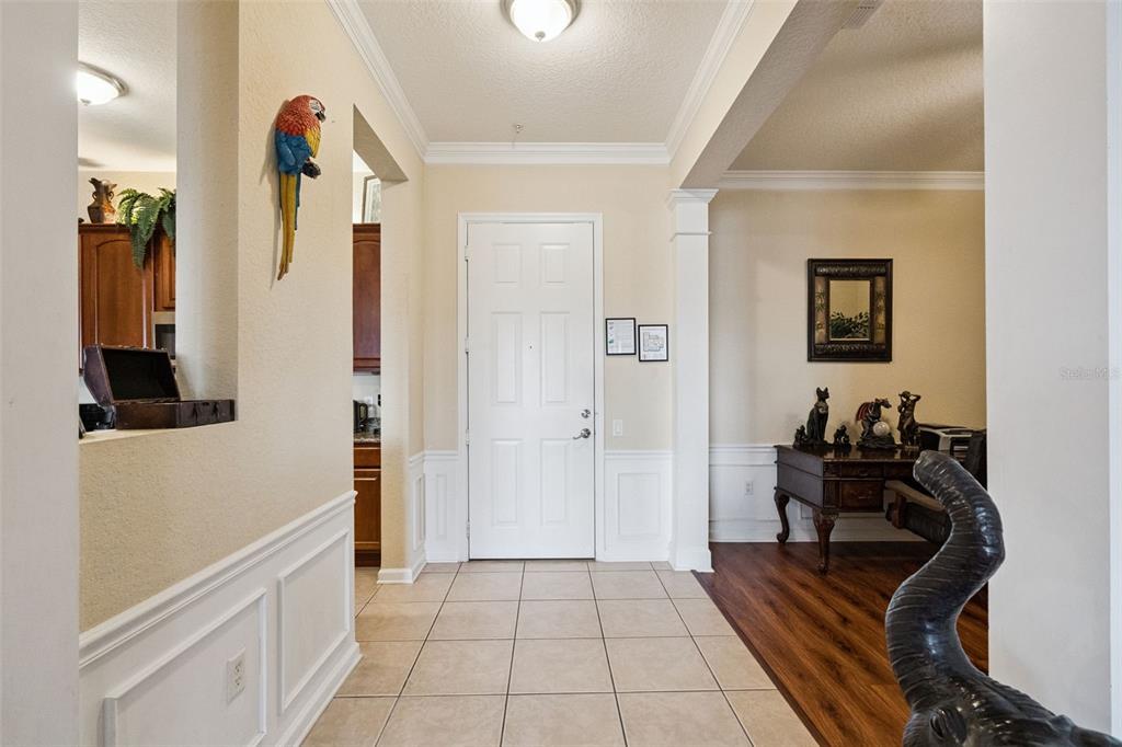 Entry Foyer:Welcoming indoor foyer with neutral tile flooring, crown molding, detailed wainscoting, and seamless flow into adjacent rooms.