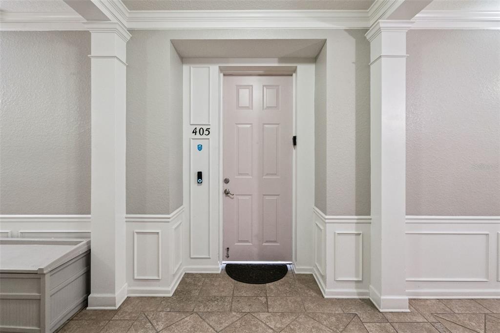 Unit Entrance:Private condo front entrance framed by decorative white columns, detailed wainscoting, and smart video doorbell integration.