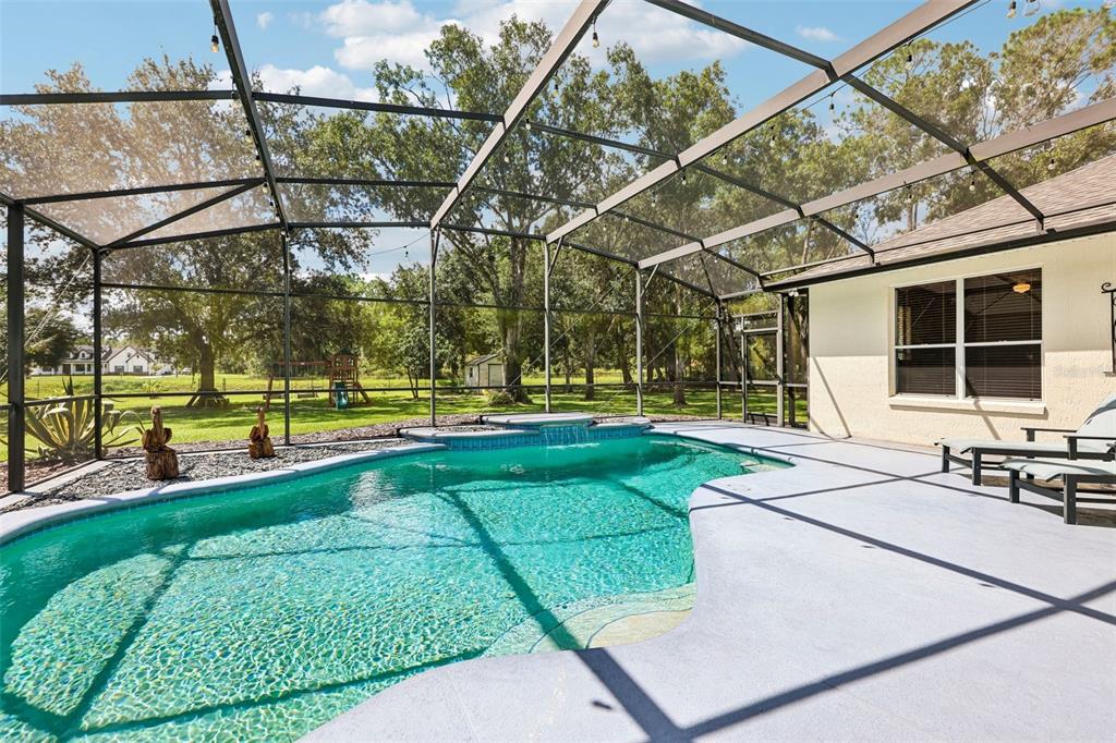 Step outside where the covered back patio and IN-GROUND POOL with WATERFALL FEATURE are enclosed within a screened lanai.