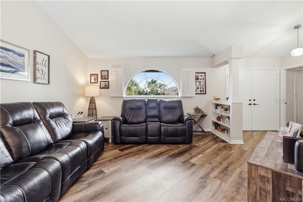 SPACIOUS LIVING ROOM- Comfortable living room featuring newer luxury vinyl flooring, vaulted ceiling & a beautiful arched window w/plantation shutters.
