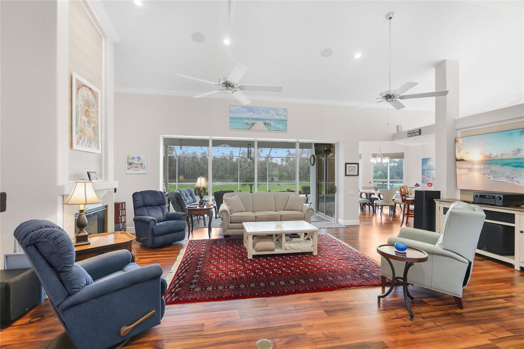 The great room has high ceilings, luxury vinyl plank flooring, six-inch crown molding, ceiling fans, and a poolside lake view