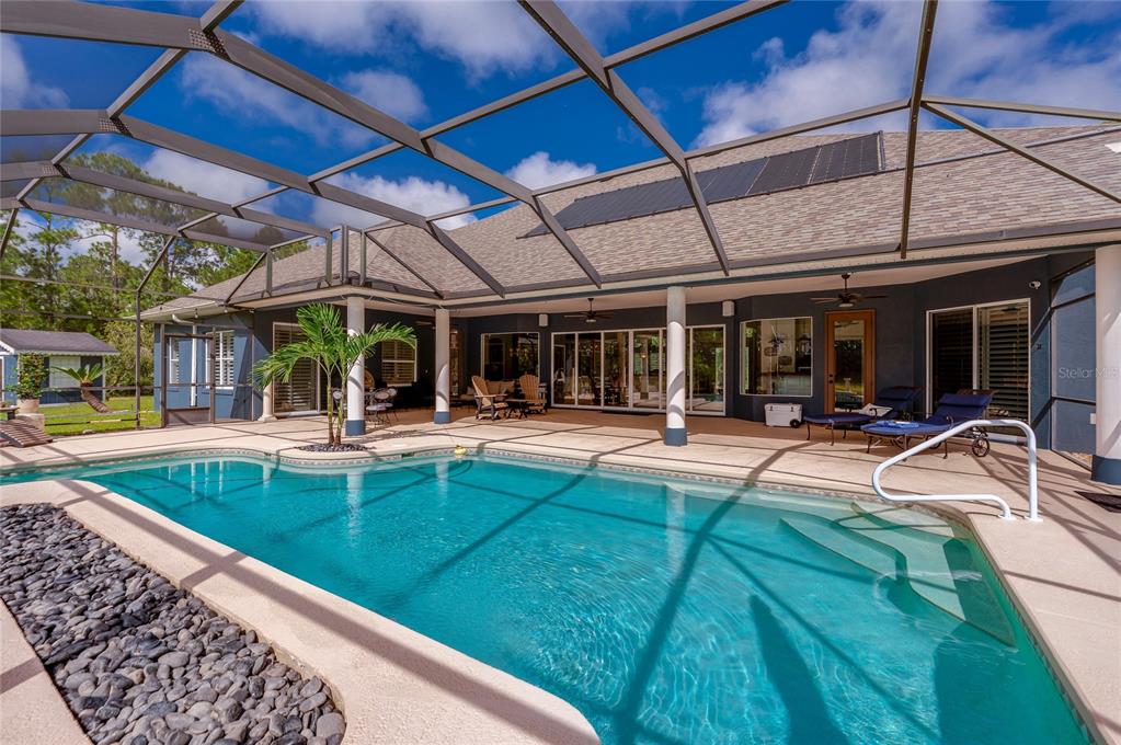 Overview of the screened pool enclosure showcasing roof-mounted solar panels and wide steps leading into the pool.