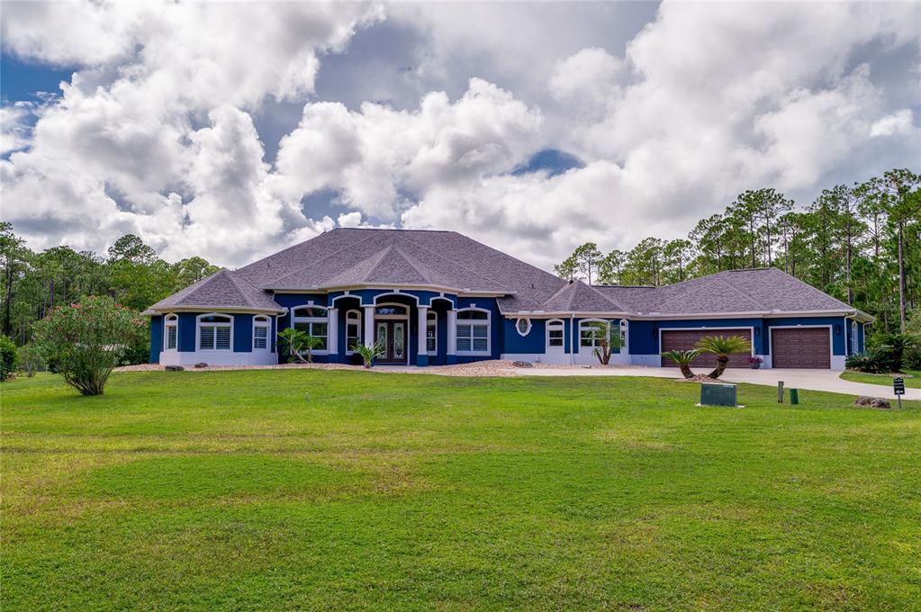 Front exterior shot of the blue home showing distinct architectural rooflines, columns, and a multi-car garage.