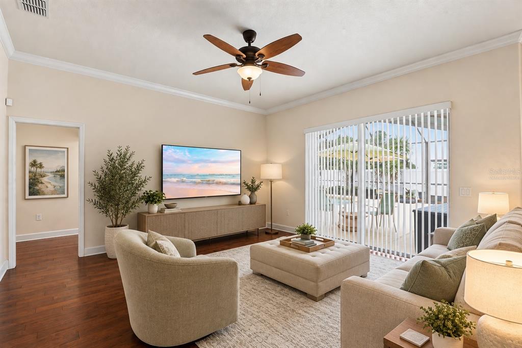 Living Room – Virtually staged to illustrate furnishing possibilities, this bright living room features warm wood flooring, crown molding, a ceiling fan, and wide sliding glass doors opening to the outdoor living and pool area.