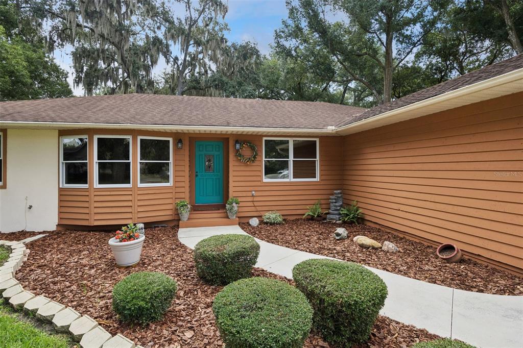 Inviting front entry with teal door, leaded glass inset, coach lanterns, and low-maintenance mulch landscaping at this Mount Dora home listed at $380,900