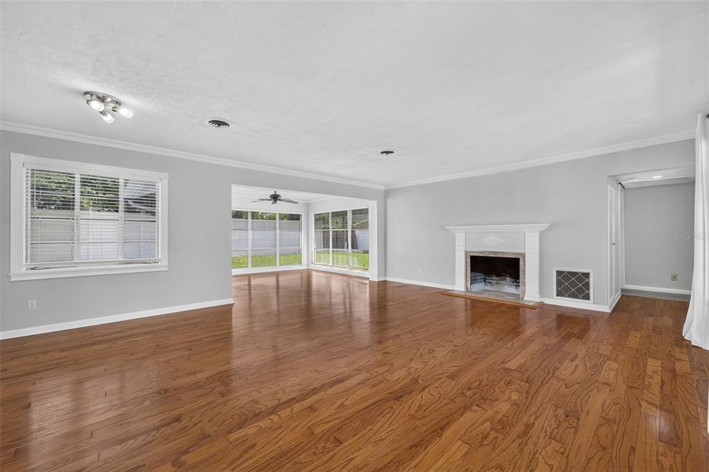 Living & Dining Area — Spacious combined living and dining area with hardwood floors, crown molding, fireplace, detailed millwork and abundant natural light from large-format windows.