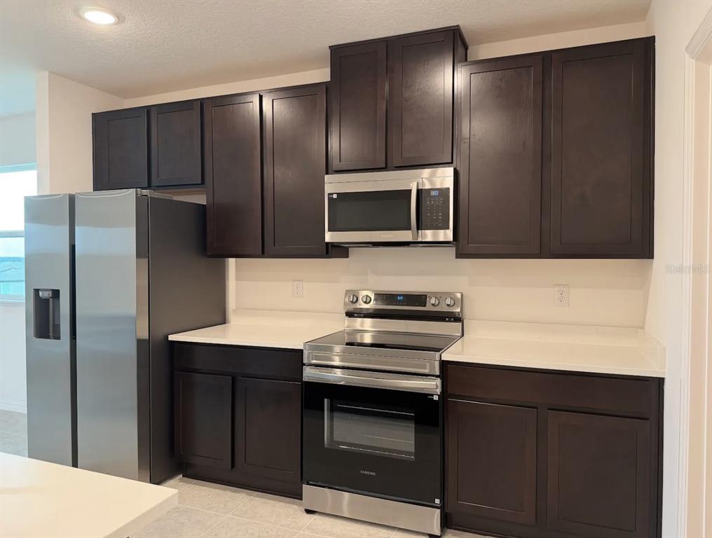 Mocha stained cabinets offer a great contrast with the quartz countertops and Samsung stainless steel appliances