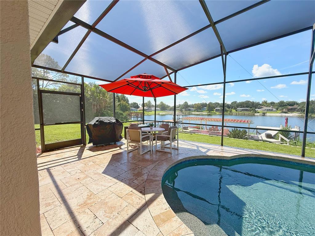 View of pool and lake and dock. Travertine flooring, pebble teak pool bottom, screened in