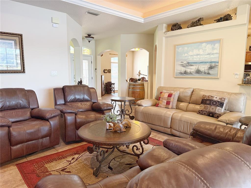 Family room with ceramic tile flooring, tray ceiling with ambient lighting, opens to Kitchen, Dining room and covered screened in lanai and pool area.,