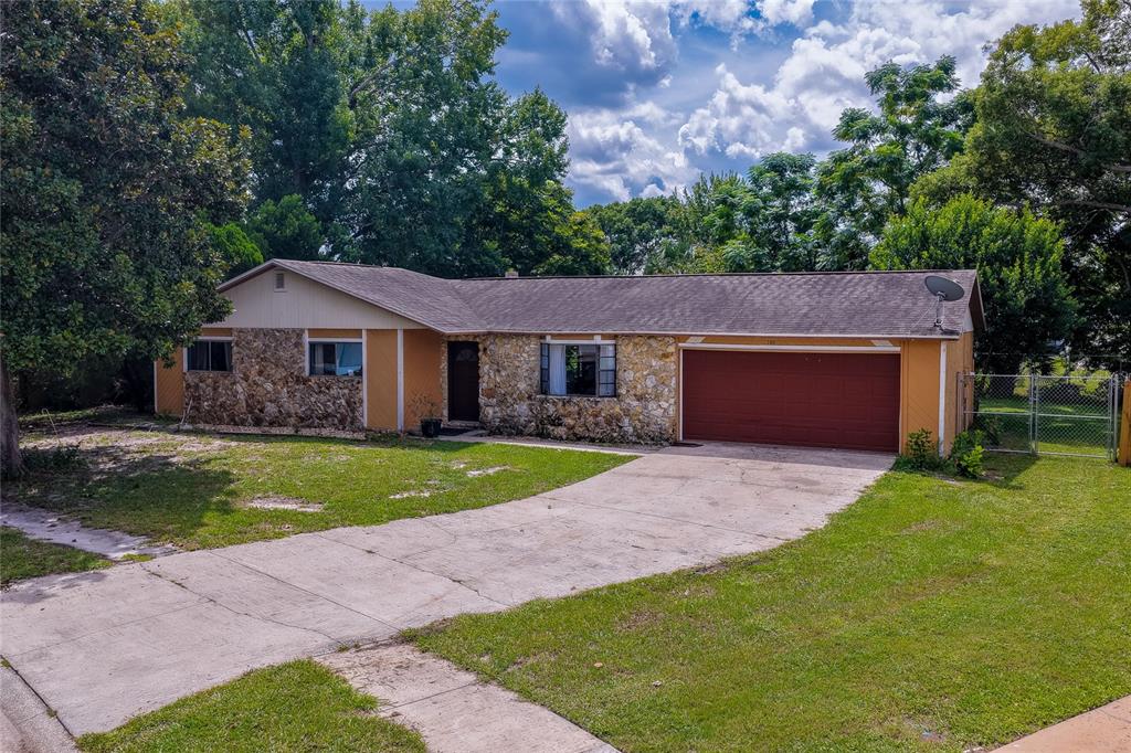 Charming single-story ranch home featuring a stone-accented facade, attached two-car garage, and an expansive paved driveway framed by lush green lawns and mature trees.