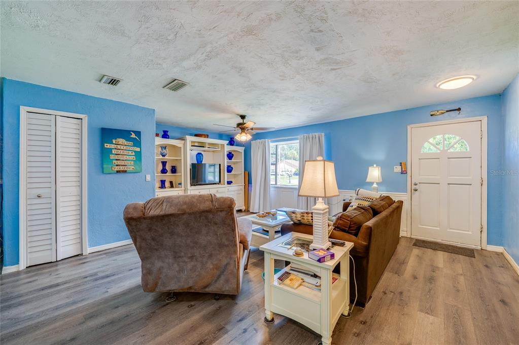 Open living space featuring light blue walls, LVP flooring, double closets, and a white front entry door with glass pane accents.