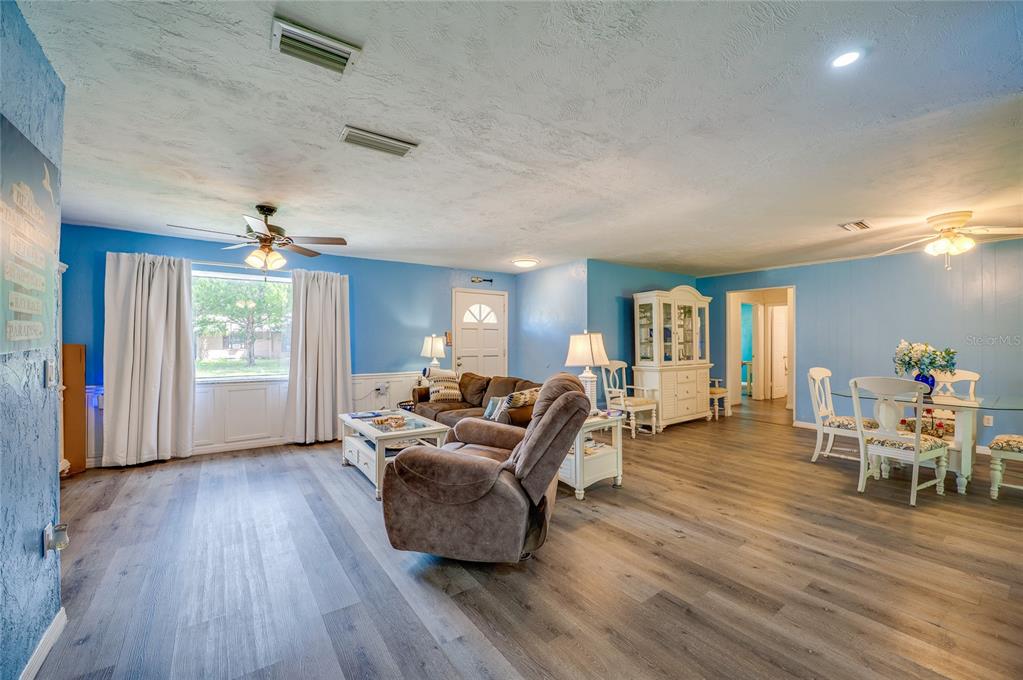 Spacious main living area displaying LVP flooring, light blue walls, a wide window bringing in natural light, and smooth transitions to adjoining rooms.