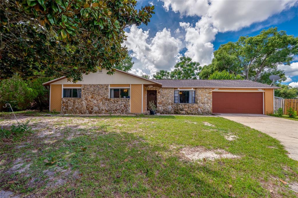 Front exterior of the ranch-style house showcasing decorative stone accent walls, a red garage door, concrete driveway, and front lawn.