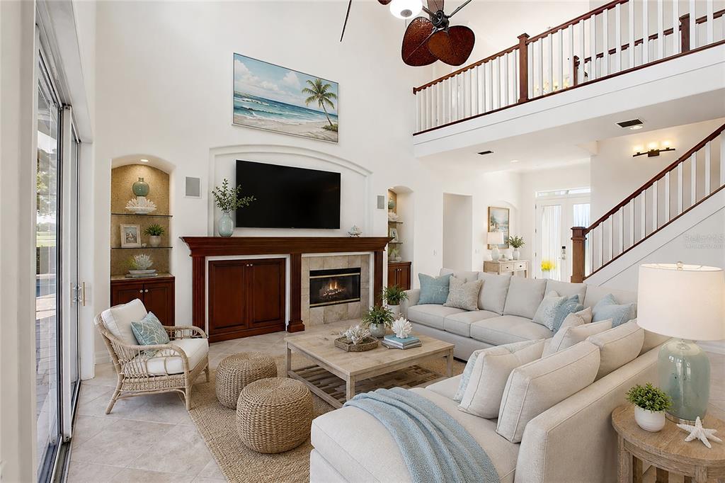 This photo is virtually staged. The family room features soaring cathedral ceilings, a fireplace with mantel, and sliding glass doors opening to the lanai, while flowing seamlessly into the kitchen for comfortable everyday living and entertaining.